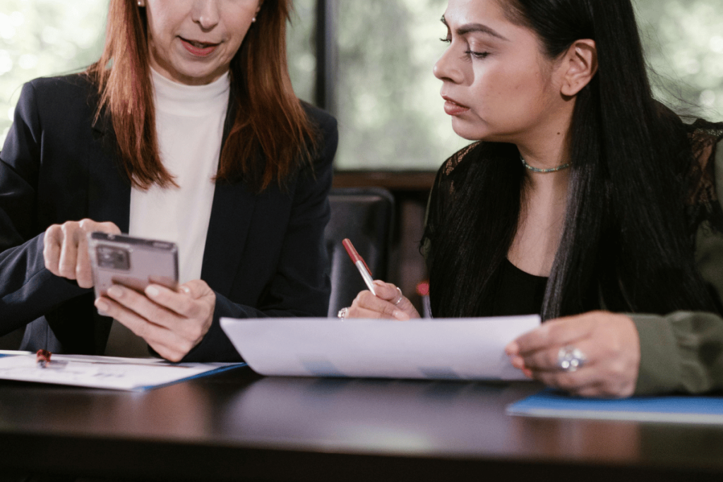 Two professional women reviewing documents, one holding a smartphone.