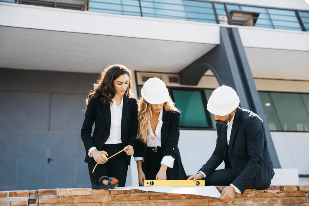 Three people in suits and hard hats working on a building site.