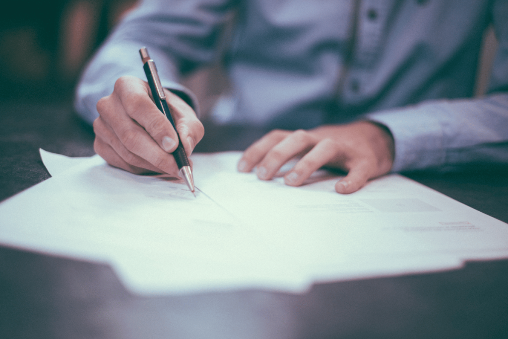 Focused shot of a hand holding a pen over a paper, ready to write or sign, with soft focus in the background.